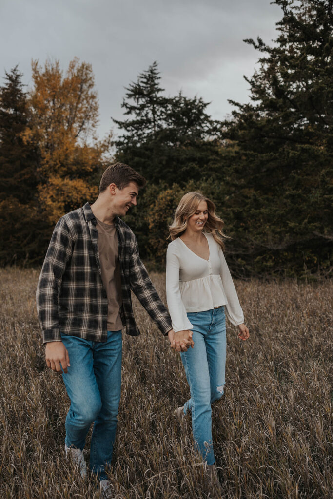 Tess and Cole playfully running through a field for their park engagement photos in Sioux Falls SD