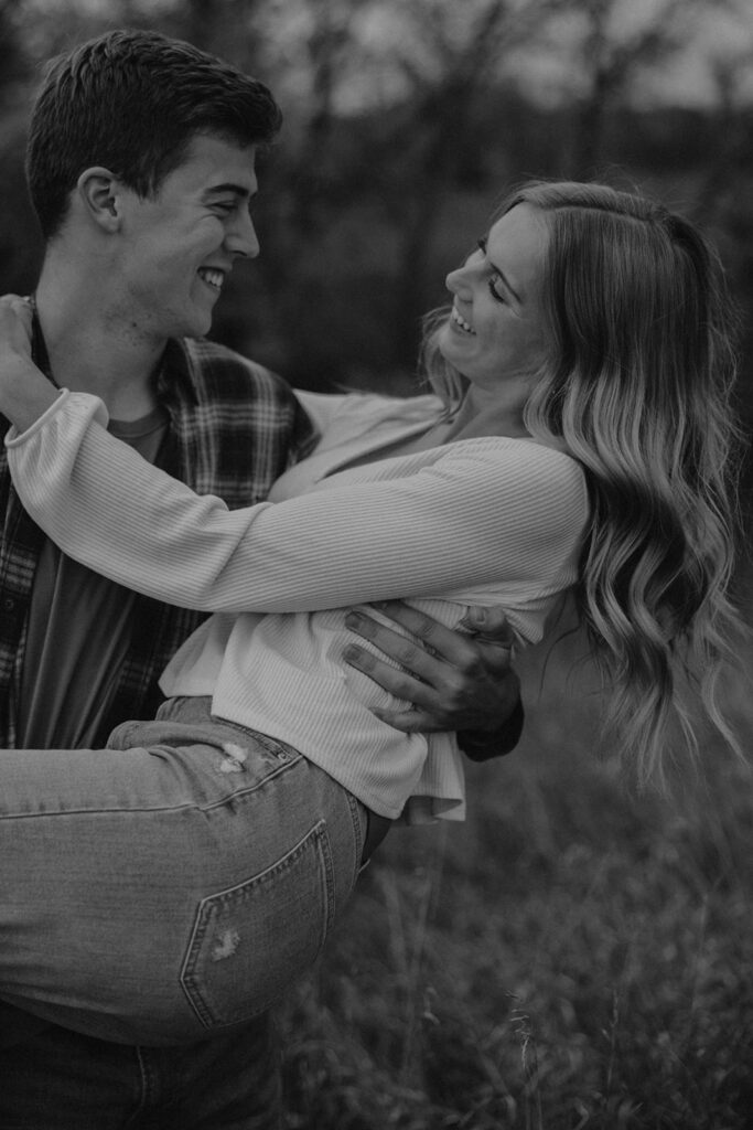 Tess and Cole hugging in a grassy field in Sioux Falls, surrounded by vibrant fall foliage for their park engagement photos