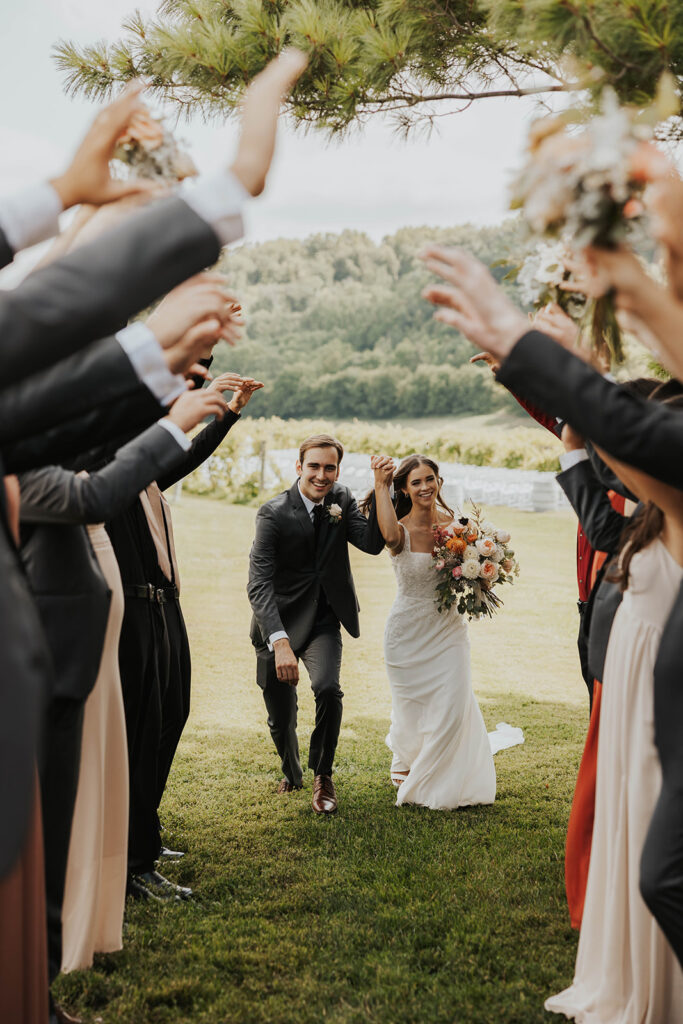 bride and groom running through a hand tunnel created by the wedding party