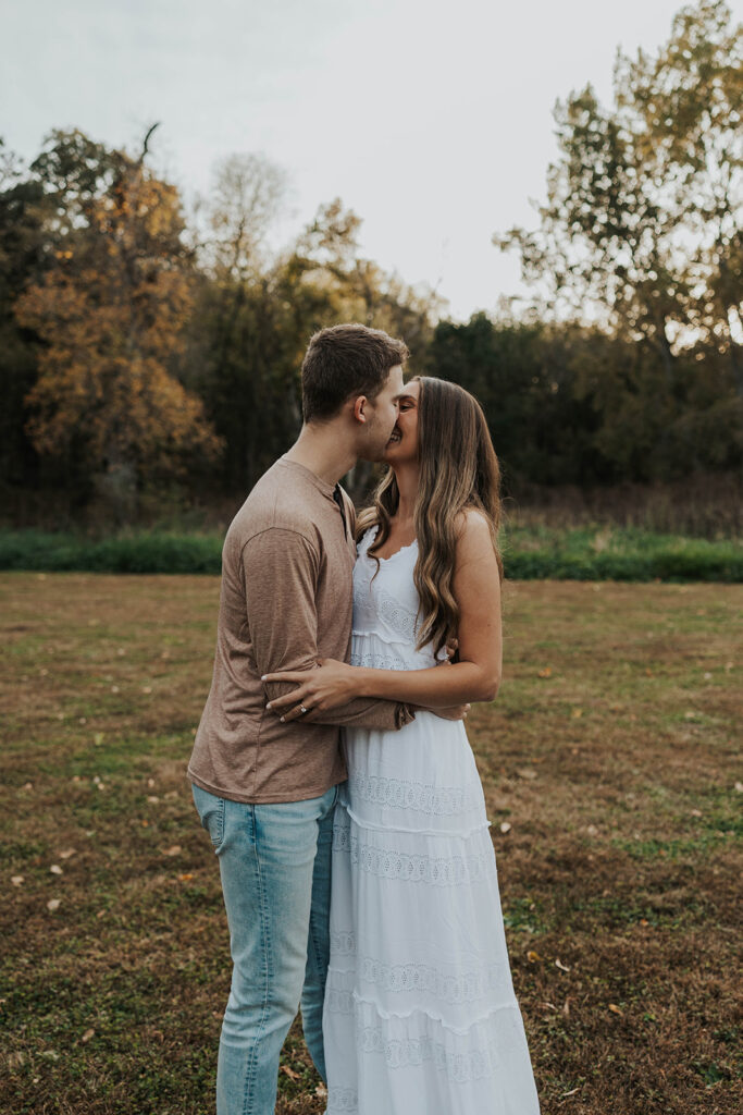 Sienna and Wyatt kissing each other playing around in a park for their fall engagement session