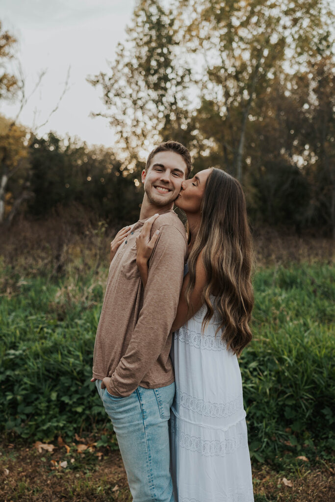 Sienna and Wyatt kissing each other playing around in a park for their fall engagement session