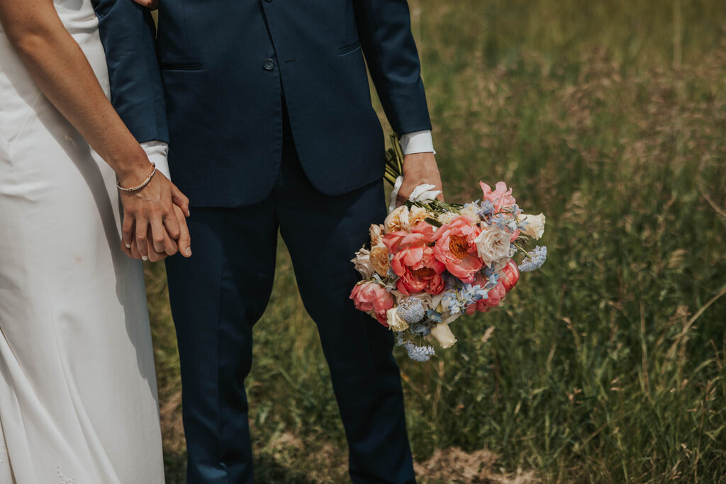 close up of bride and groom holding hands and groom holding a colorful wedding bouquet