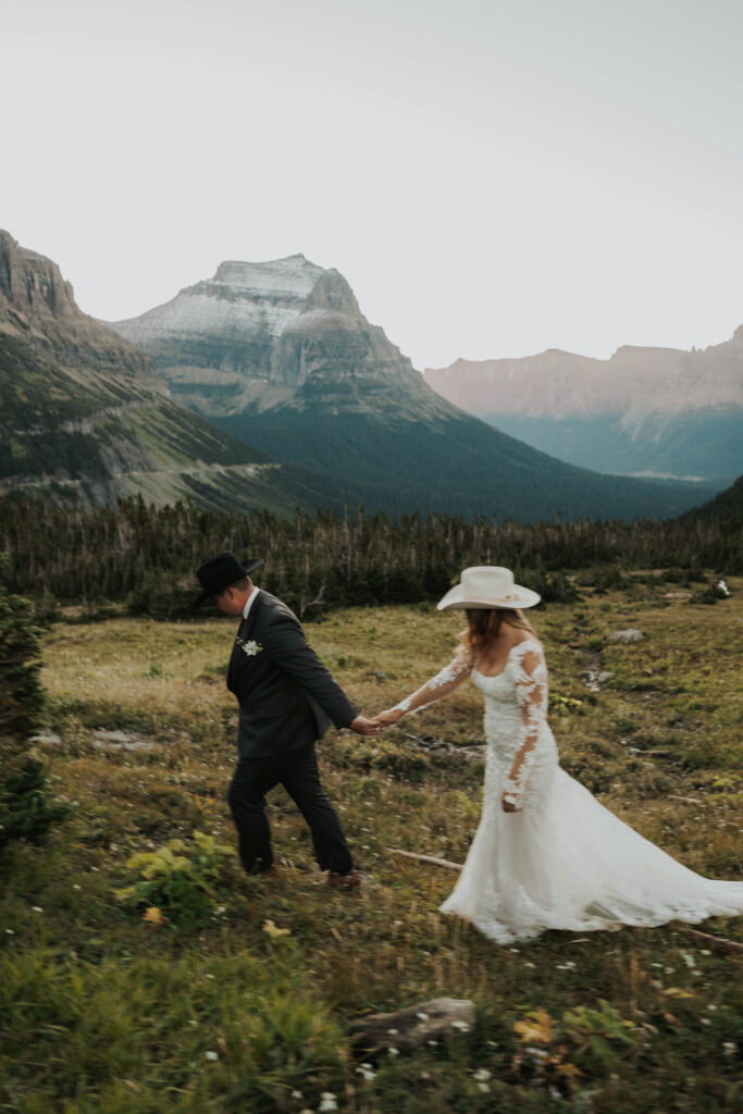 A couple holding hands and walking in front of a mountain at Glacier National Park