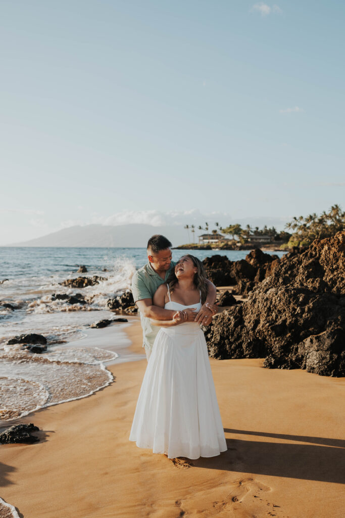 Couple laughing together in front of rocks on Po'olenalena Beach in Maui, Hawaii. 