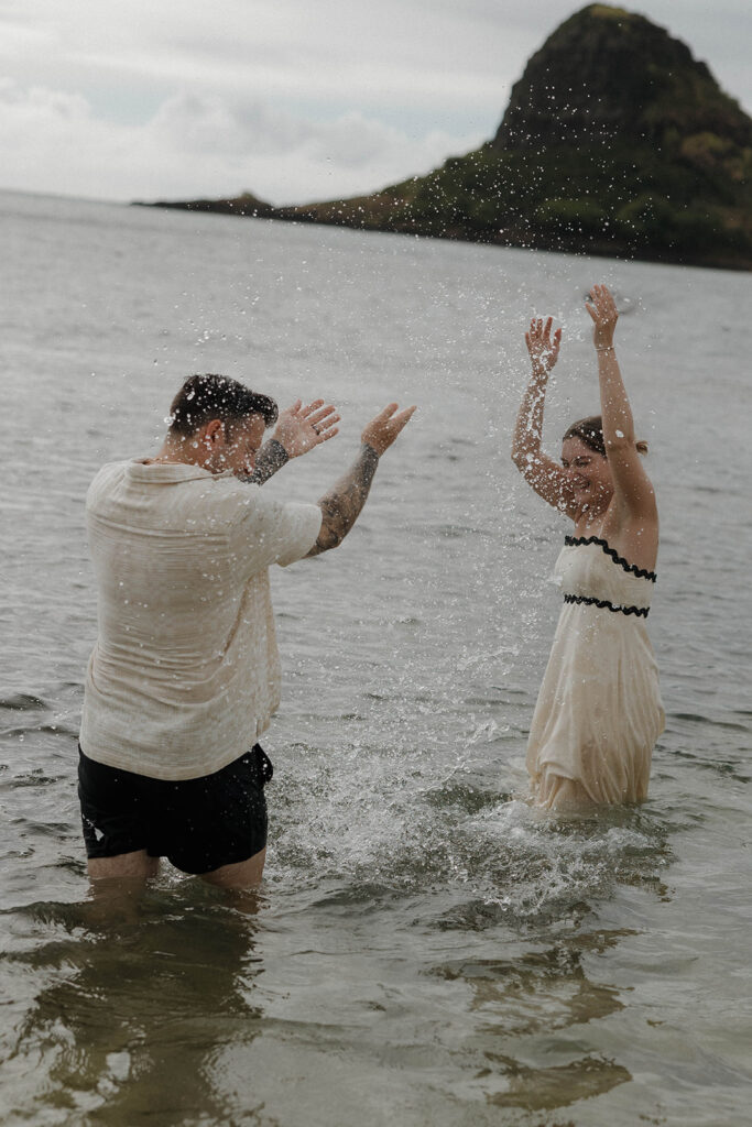 playful candid couples photo playing in the ocean and splashing water