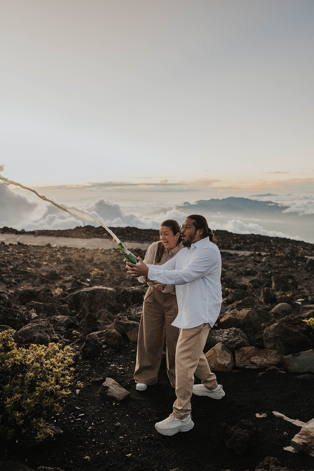 a couple popping champagne on top of a mountain at one of Maui's best engagement photo locations
