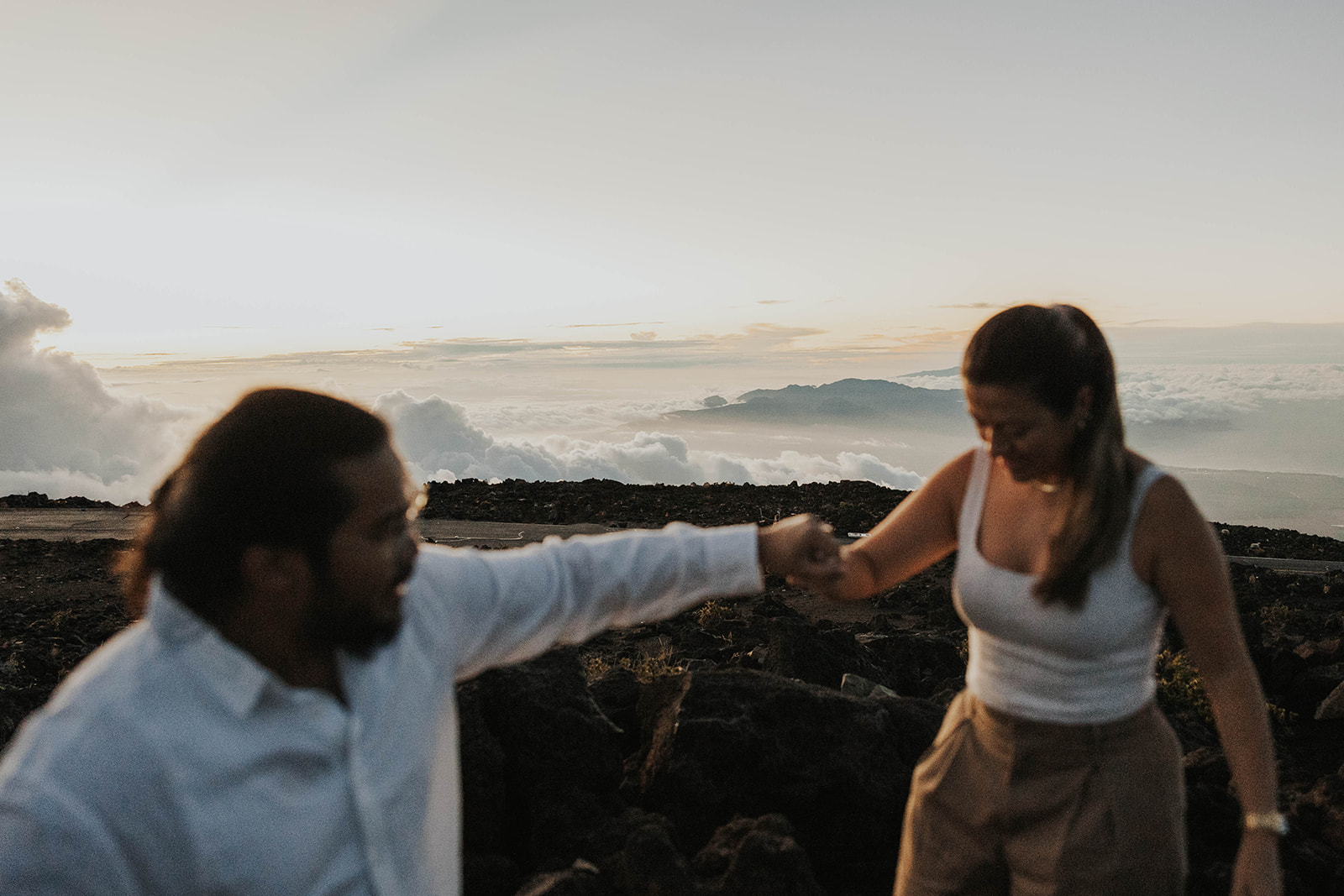 a man helping a woman over the rocks with the clouds behind them 