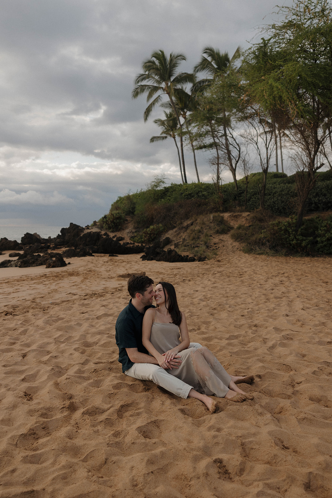 a couple sitting together at the beach, captured by a Maui proposal photographer