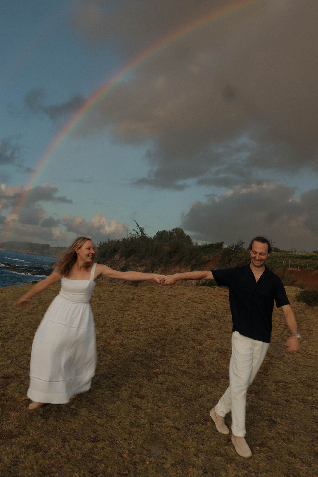 a couple holding hands with a rainbow behind them during their Maui proposal photos