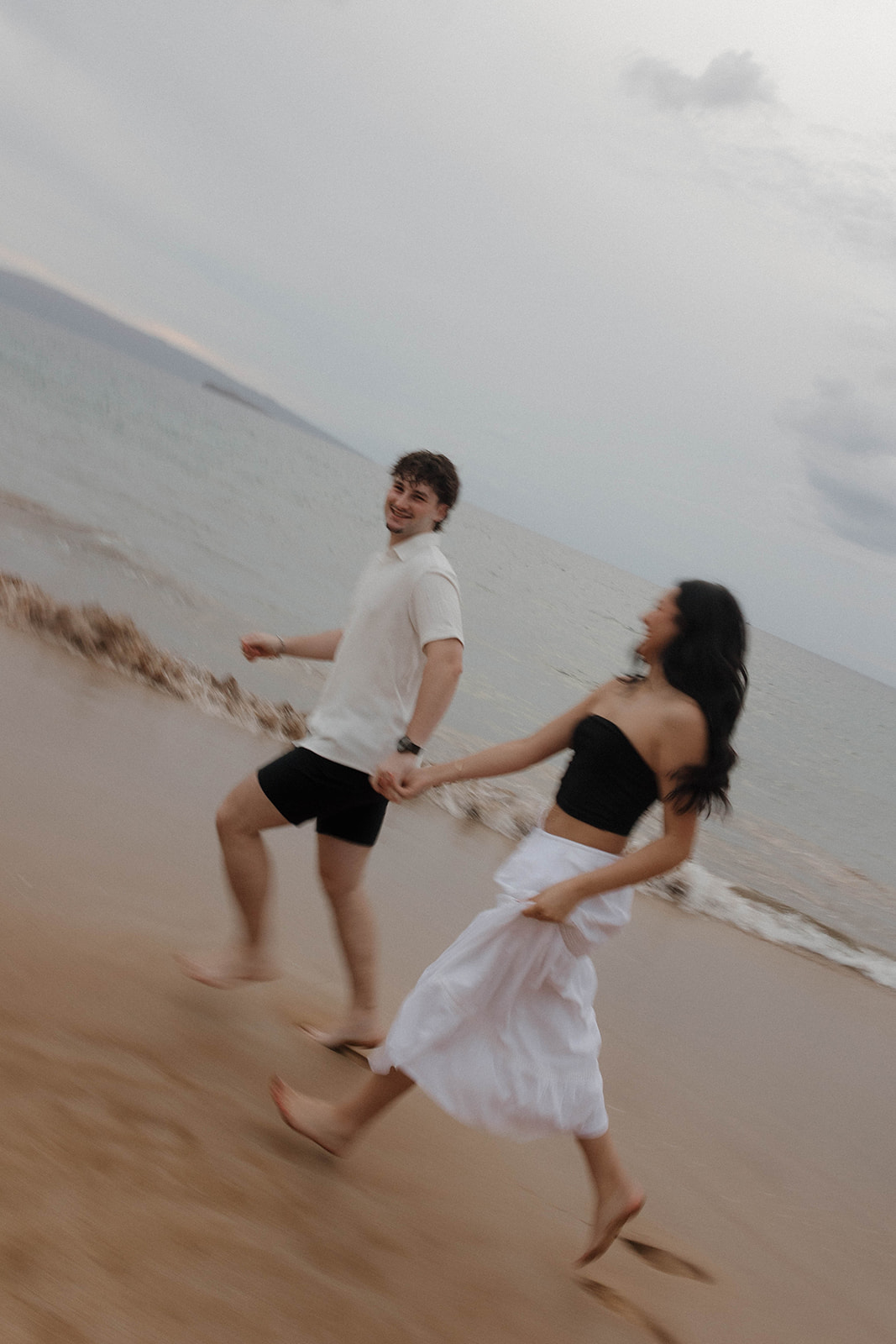 a couple running on the beach, while wearing flowing engagement photo outfits 
