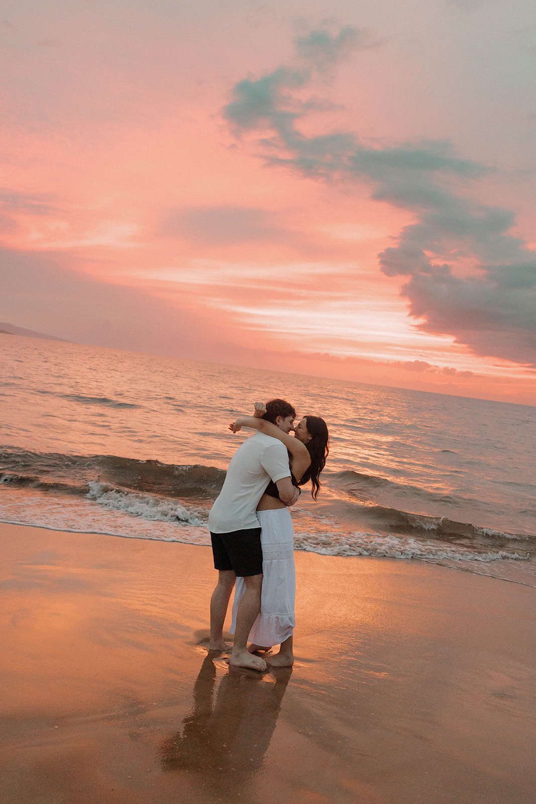 a couple hugging on the beach with an epic sunset behind them in Hawaii