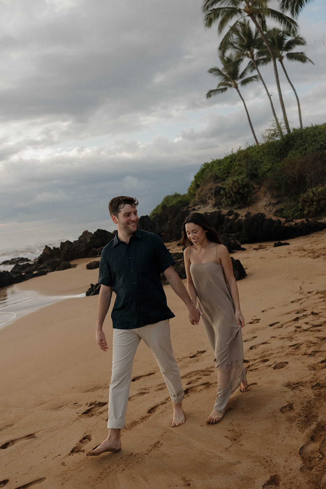 a couple, in the perfect engagement photo outfit, walking together on the beach 