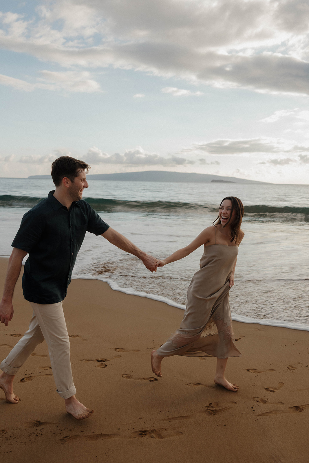 a couple running on the beach while featuring what to wear for engagement photo outfits in Hawaii