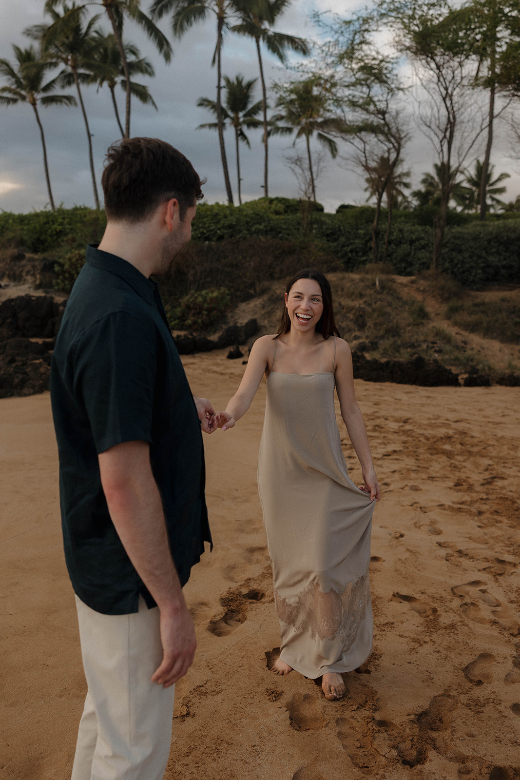 a woman in a tan colored dress and a man matching in a black shirt and tan pants for engagement photos in Hawaii 