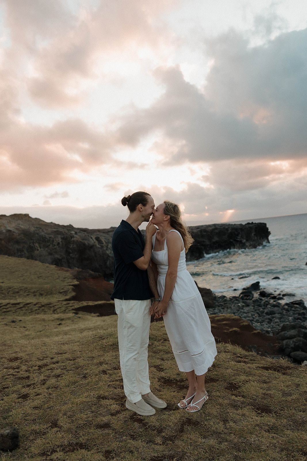 a couple kissing as they stand on a cliff in Hawaii featuring what to wear for engagement photos