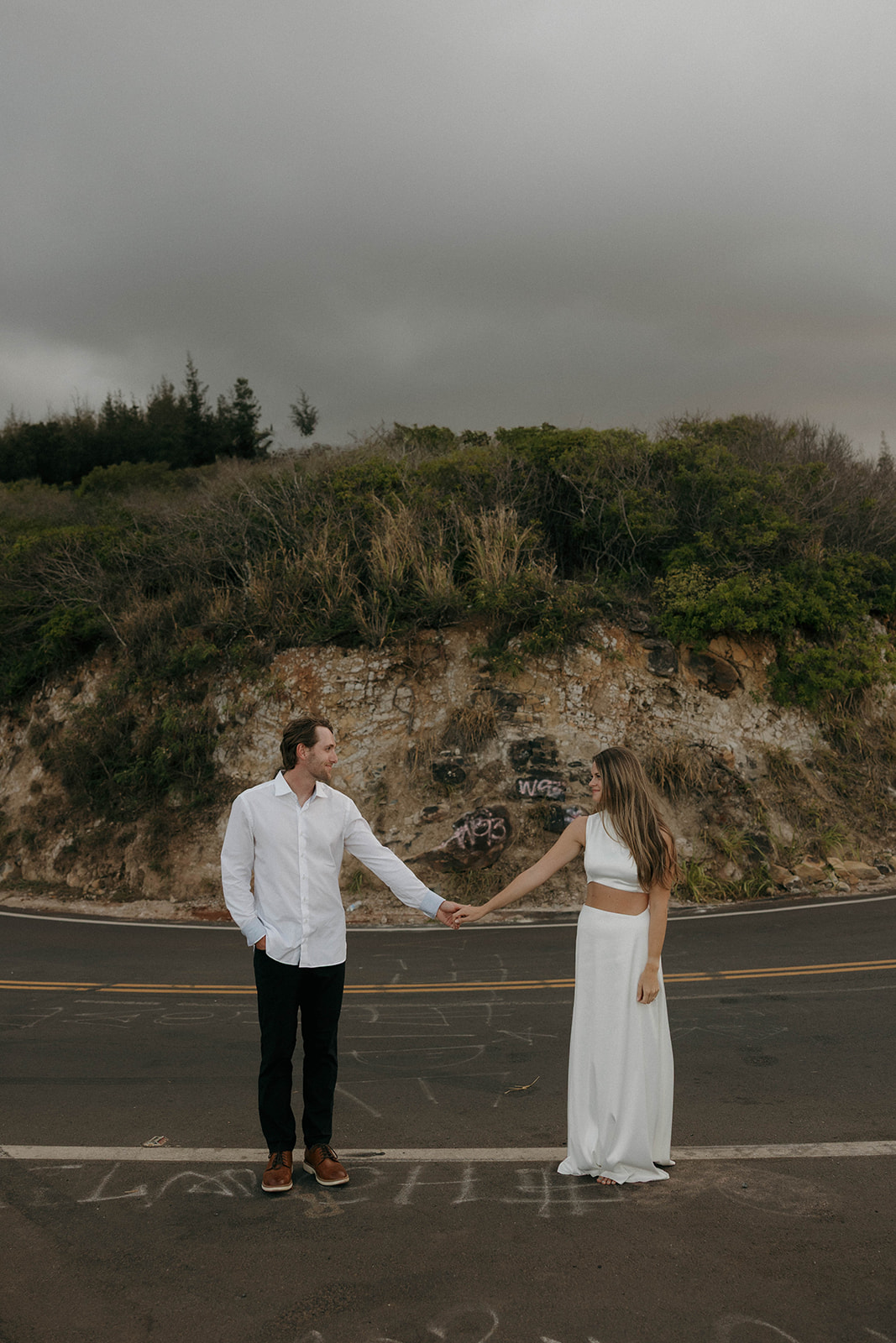 a couple holding hands as they stand on a road during Maui engagement photos 