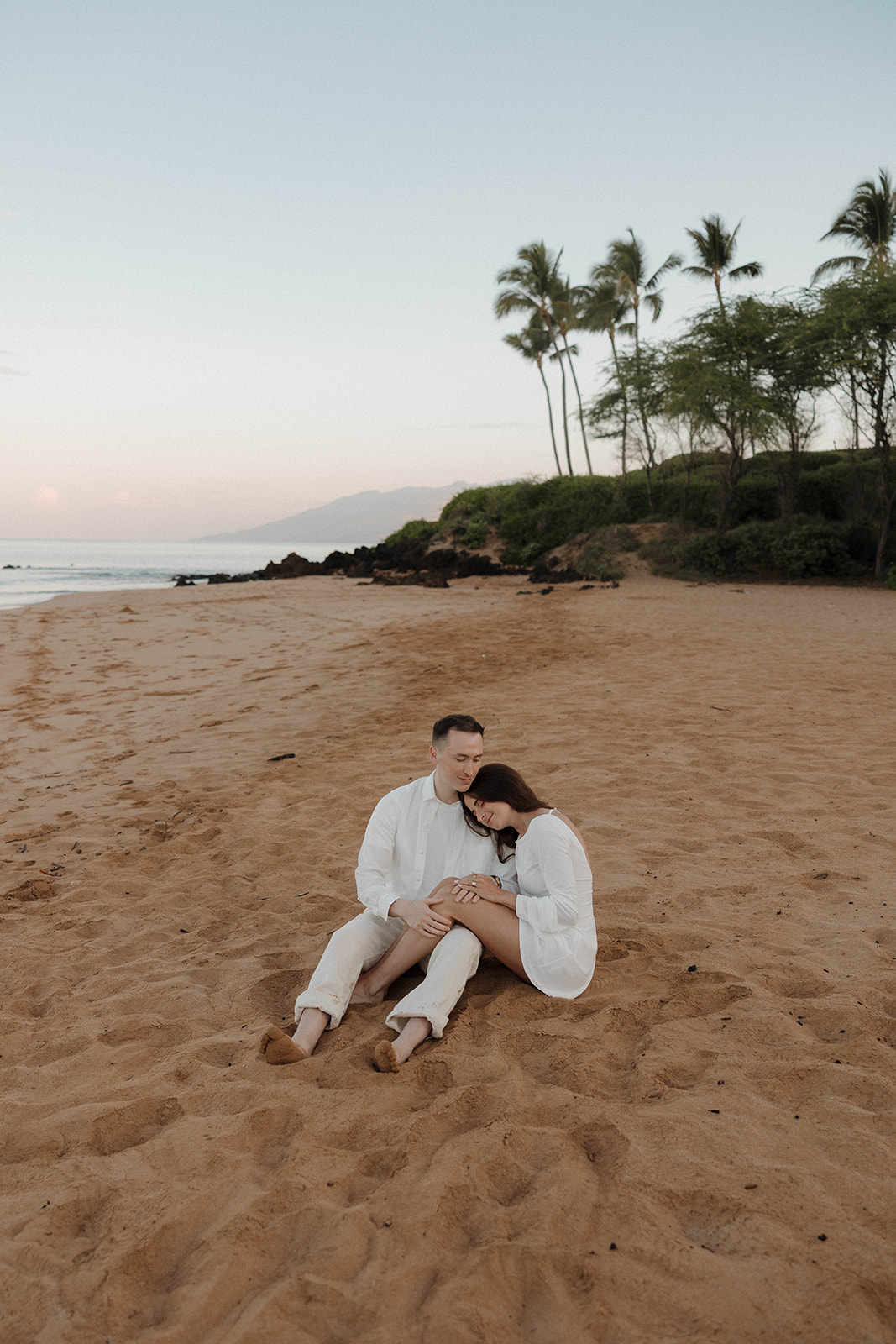 a couple sitting in the sand together for their Hawaii engagement photos 