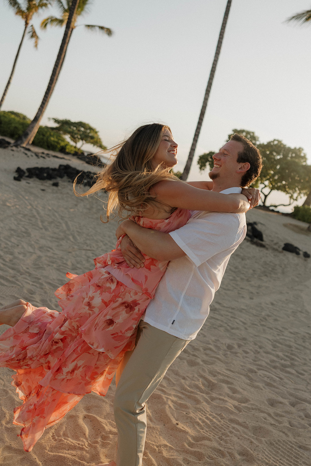 a woman in a bright floral dress and a man spinning her around in Hawaii for engagement photos