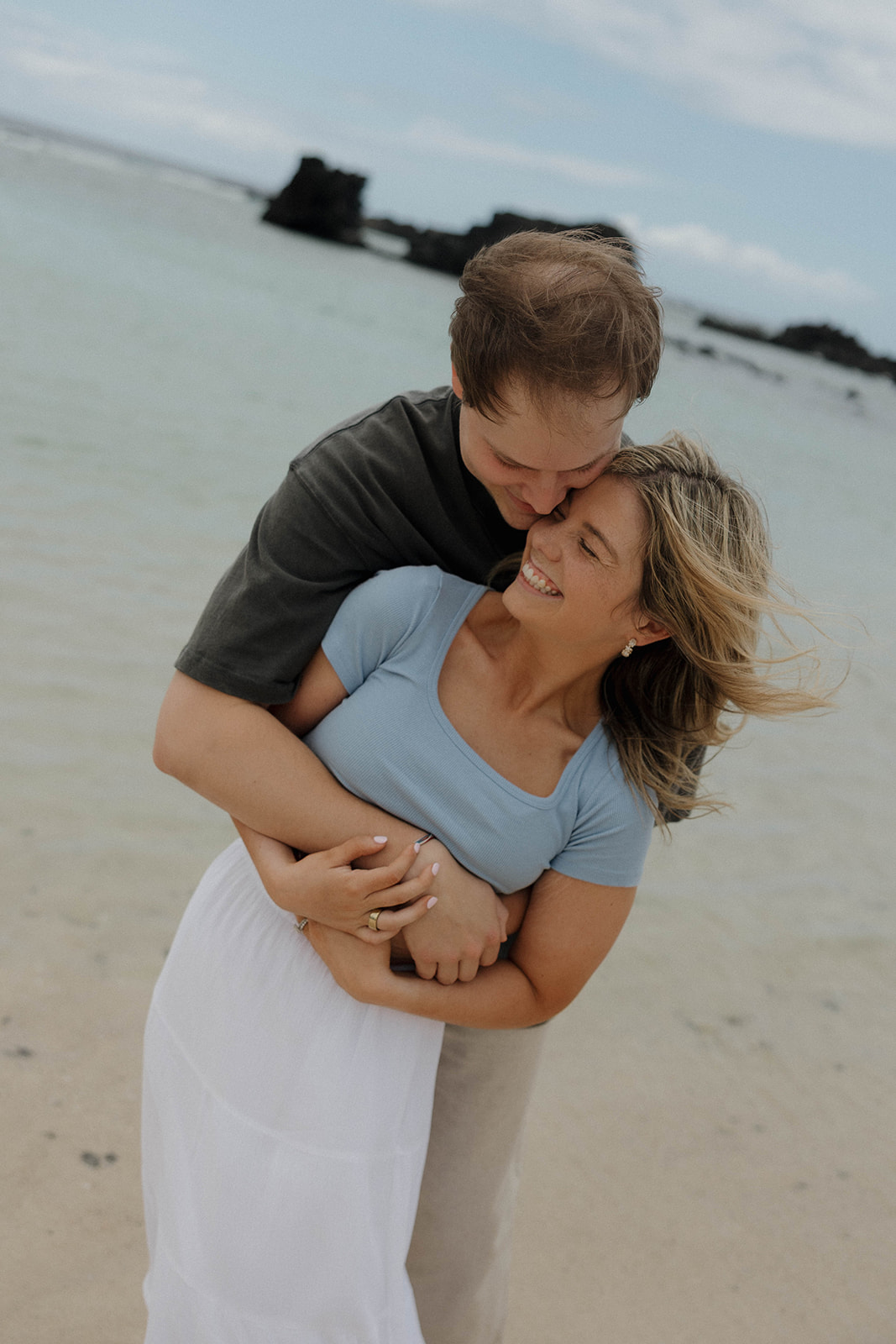 a man hugging a woman from behind as they stand on the beach together 