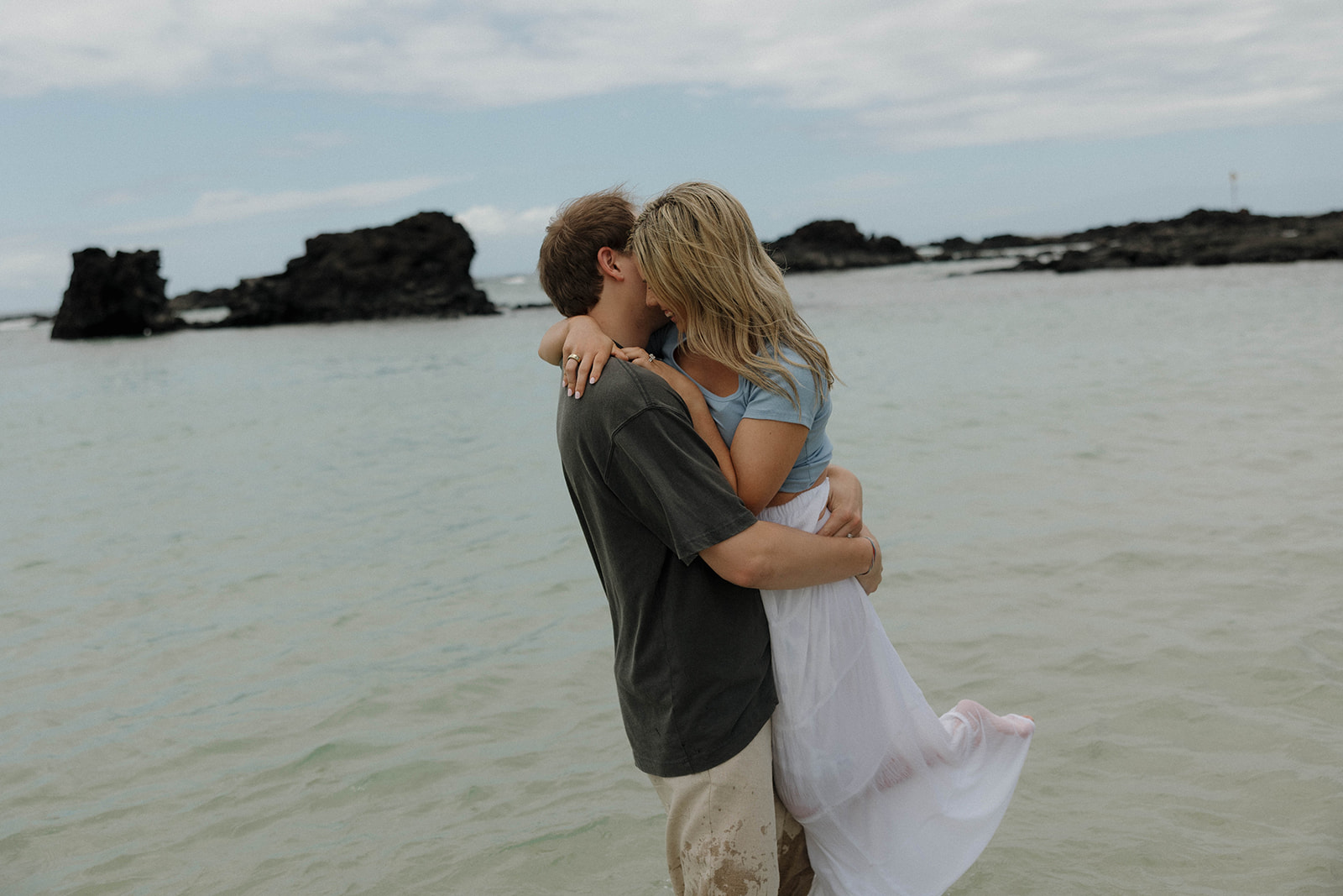 a man holding a woman as they stand in the ocean for their Hawaii engagement photos