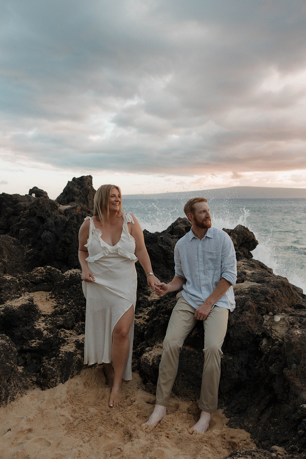 a couple standing by the rocks as waves crash into them for their Hawaii engagement photos