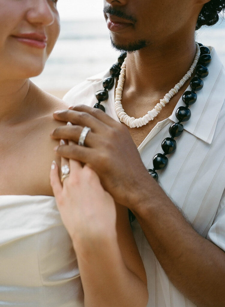 An elegant detail photo of the bride smiling back at her groom as they hold hands over her shoulder.
