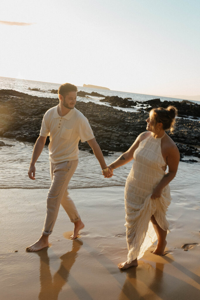 A couple walking on the sand hand in hand at sunset during their Maui beach engagement shoot and filming a Super 8 wedding video.
