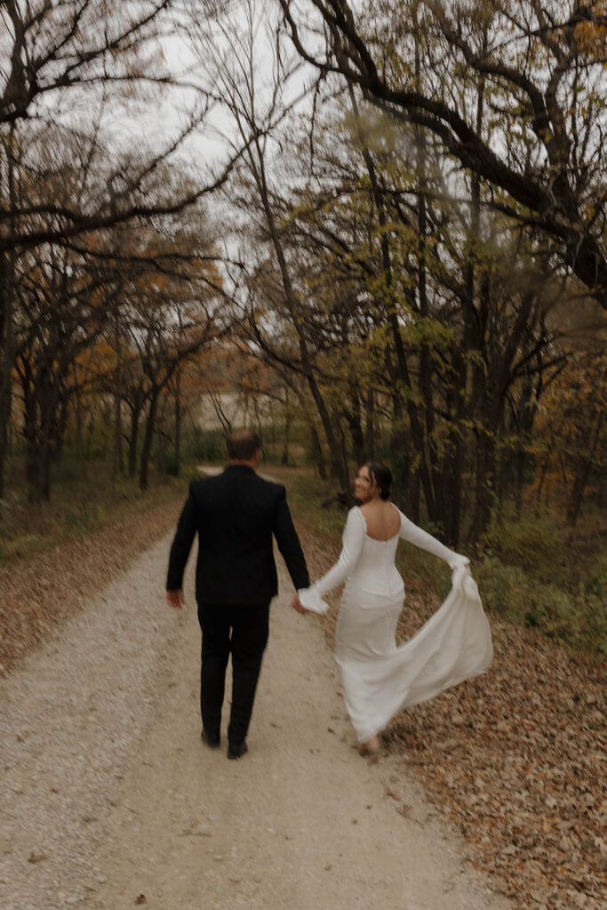 A candid photo of a married couple walking hand in hand down a dirt road during their bride and groom portraits and filming their Super 8 wedding video.