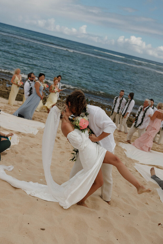 The groom dipping his bride in the middle of the aisle after their beach wedding ceremony and filming a Super 8 wedding video.