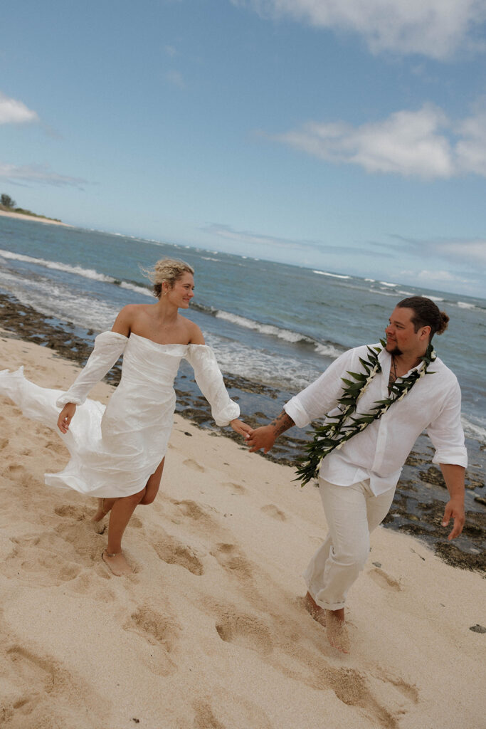 A couple running on the beach after their wedding ceremony in Maui and filming their Super 8 wedding video
