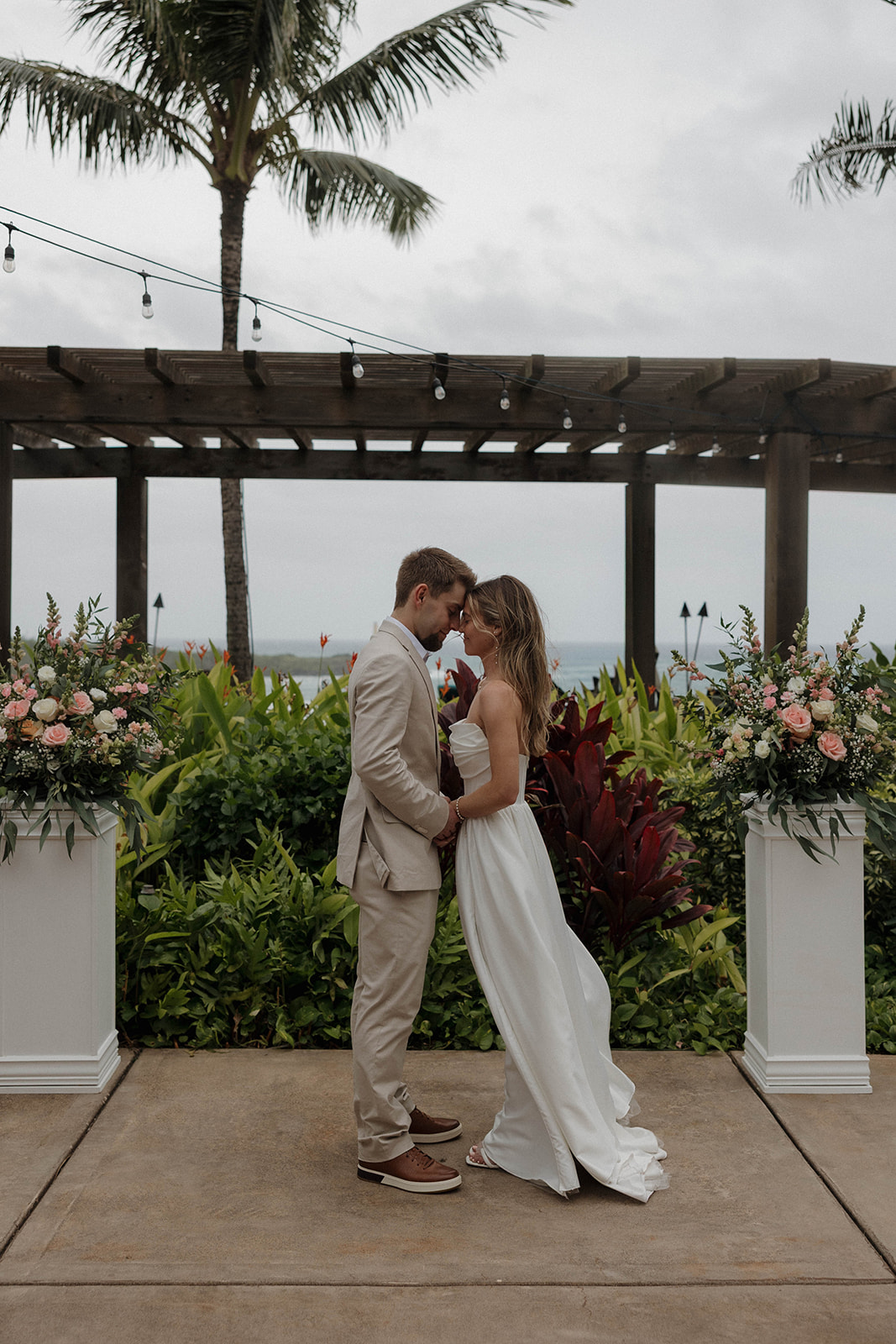 Newlywed couple sharing a quiet moment at the ceremony altar framed by tropical arrangements and coastal views.