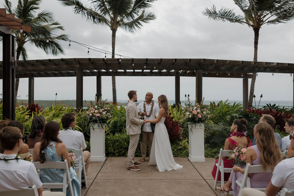 Outdoor ceremony setup overlooking the ocean with tropical florals and palm trees during a destination wedding in hawaii.