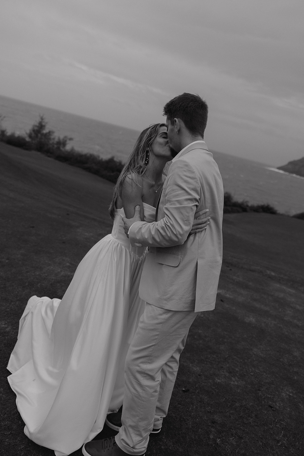 Black and white portrait of the couple kissing on a dramatic coastal overlook at a destination wedding in hawaii.