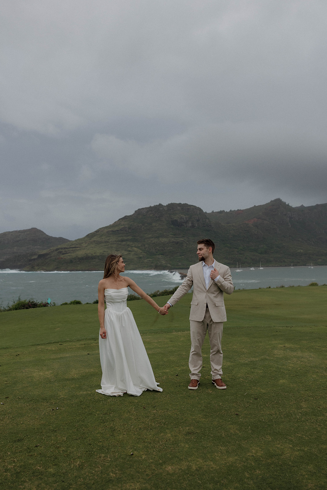 Newlywed couple holding hands on a coastal cliff overlooking the ocean at a destination wedding in hawaii.