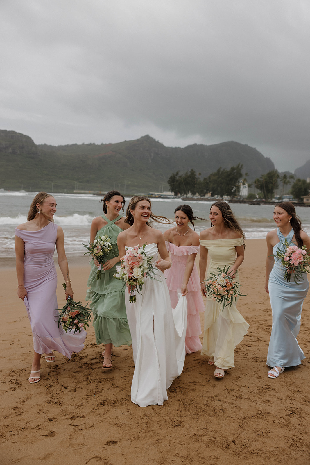 Bride walking along the shoreline with her bridesmaids in pastel dresses during a destination wedding in hawaii.