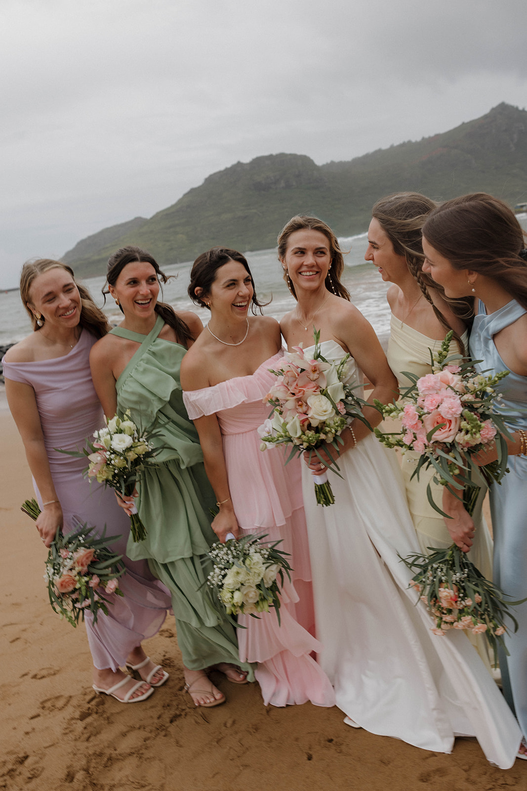 Bride standing an the beach with her bridesmaids in pastel dresses during a destination wedding in hawaii.