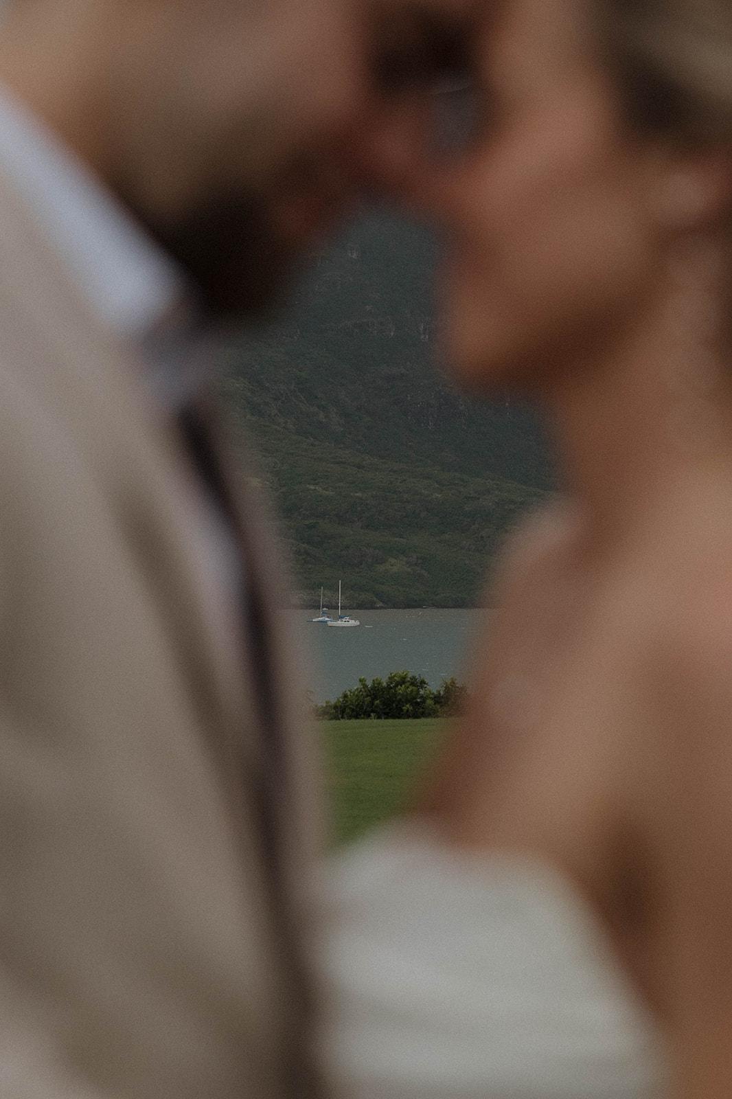 Intimate close-up of the couple kissing with the ocean and sailboats blurred in the background.