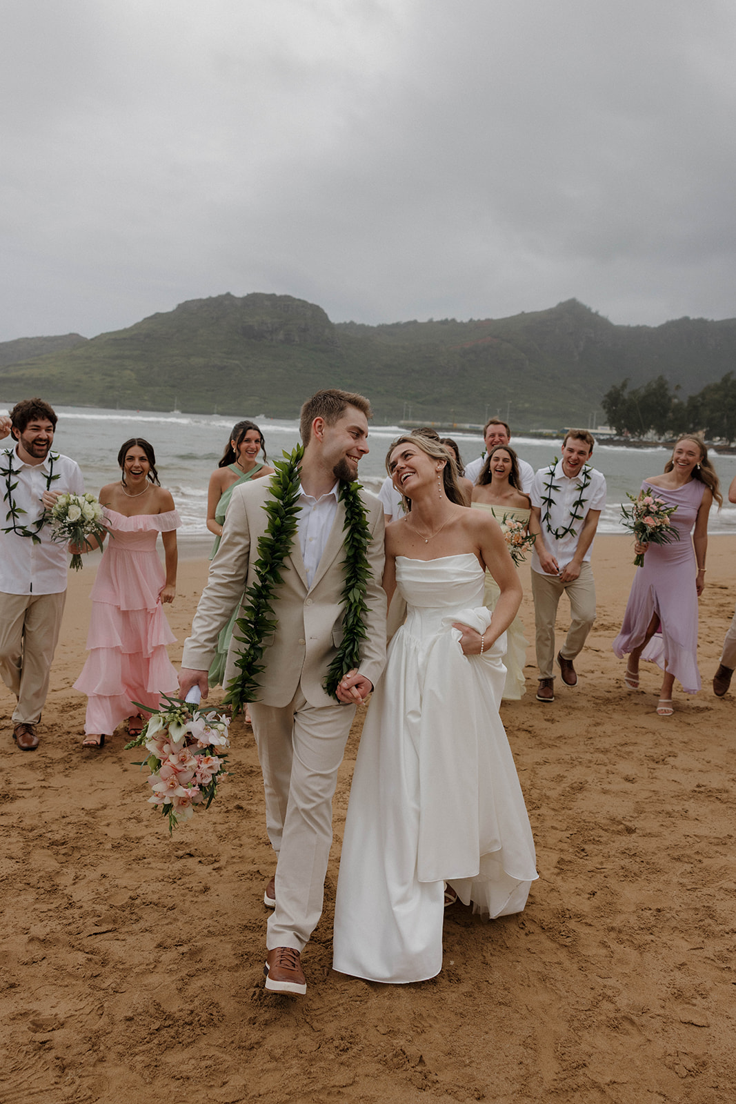 Joyful bridal party walking along the beach behind the bride and groom celebrating together by the water.