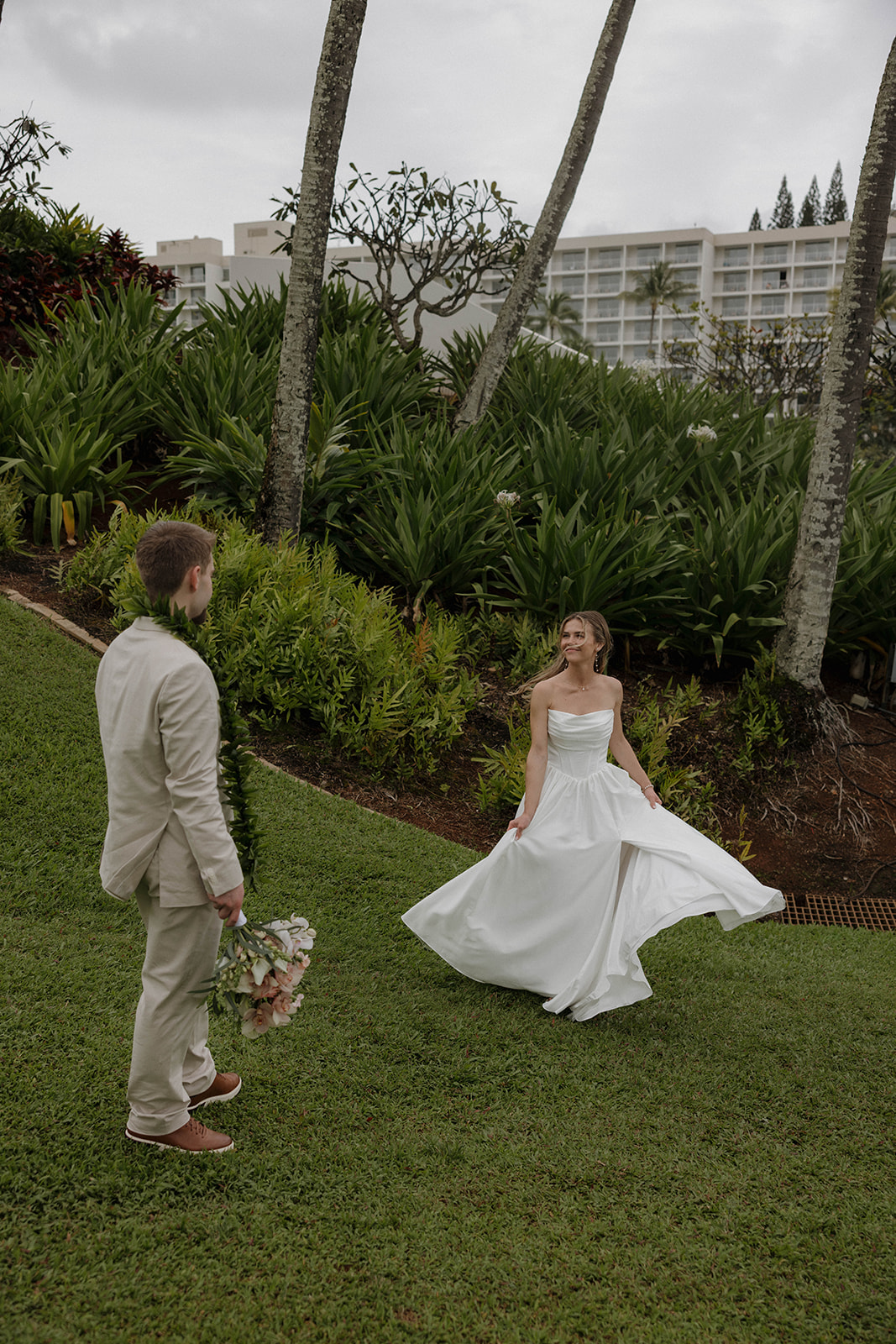 Bride and groom walking through a lush resort lawn with palm trees during a destination wedding in hawaii.
