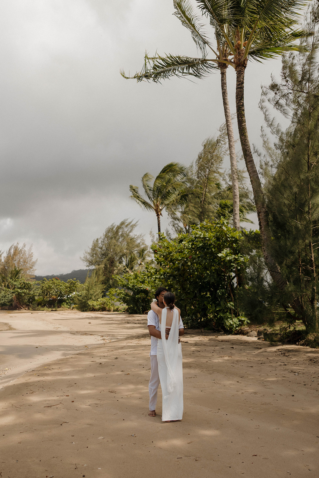 The bride and groom hugging and sharing a kiss on the beach during their bride and groom portraits in Kauai.