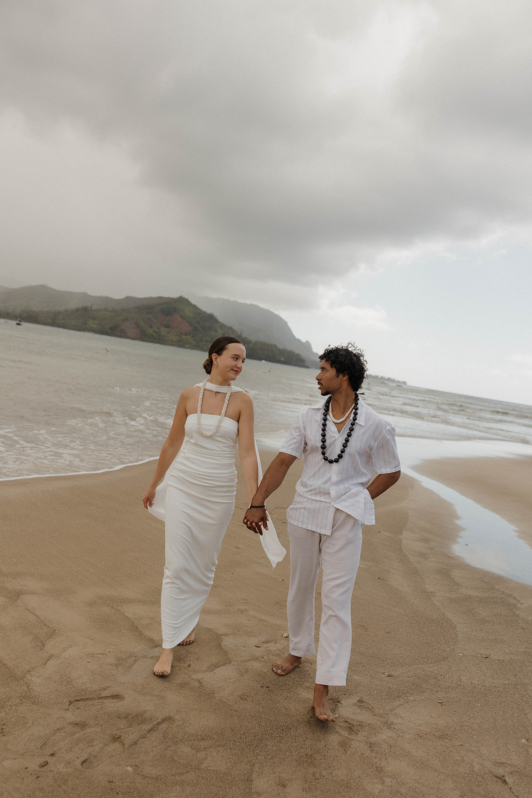 The bride and groom walking hand in hand on the beach in Kauai, after their intimate micro wedding ceremony.