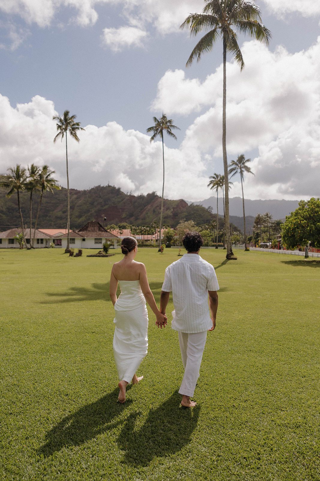 Newlyweds walking hand in hand on a grassy lawn after their micro wedding in Kauai