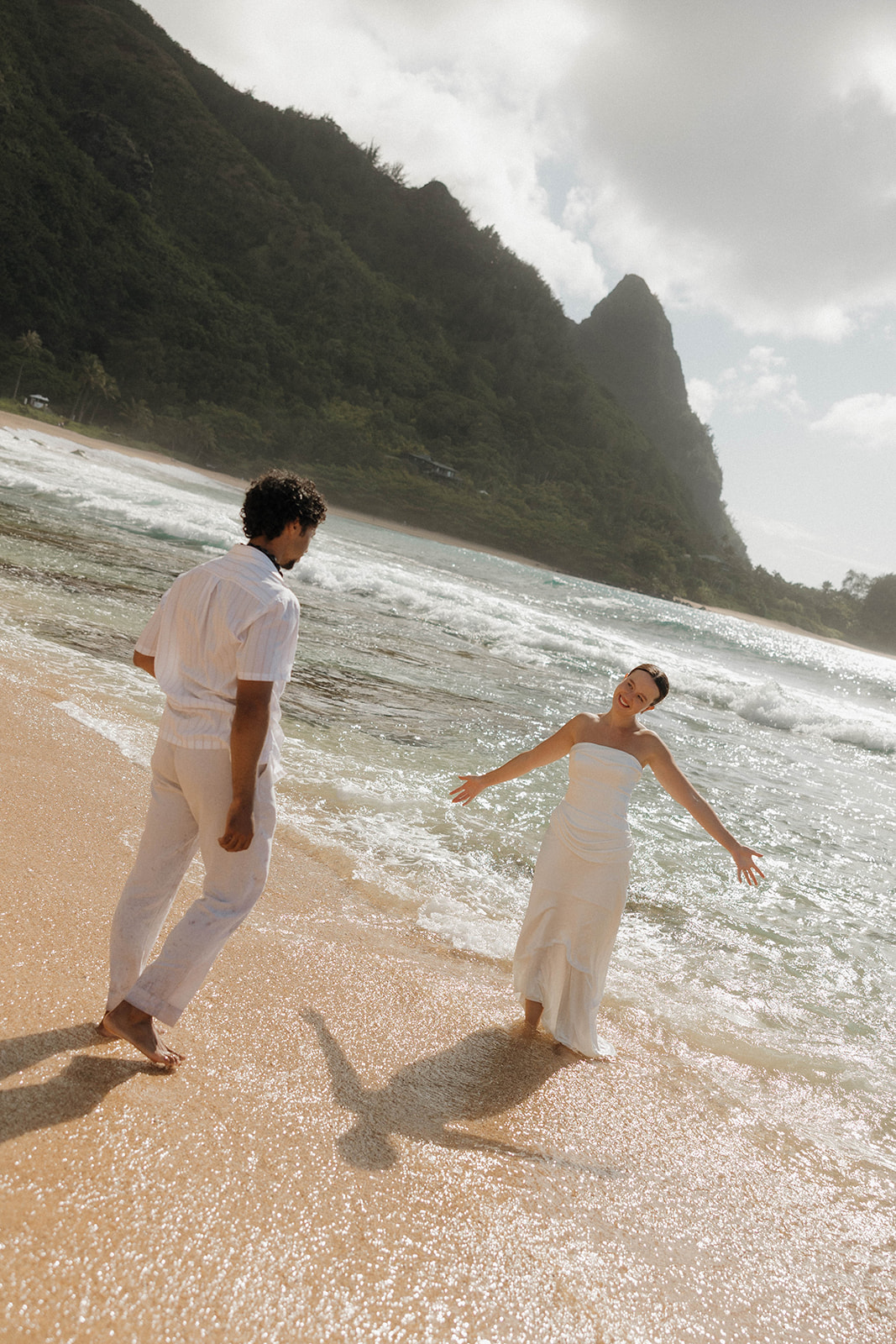 The bride and groom standing on the beach and walking around for some sunny bride and groom portraits after their micro wedding in Kauai