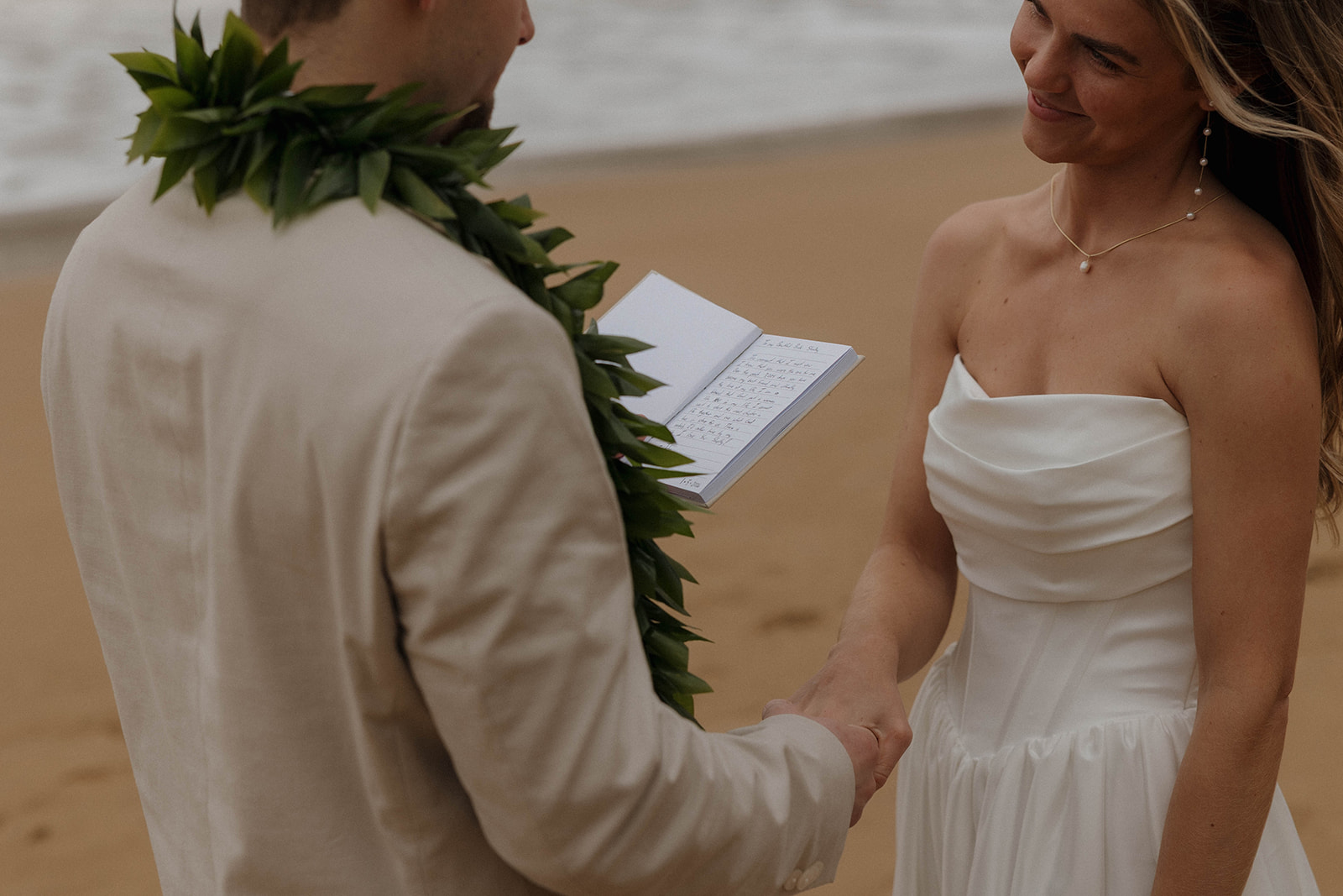 An intimate detail photo of the groom reading his vows to his wife as she smiles at him and holds his hands, during their micro wedding in Kauai