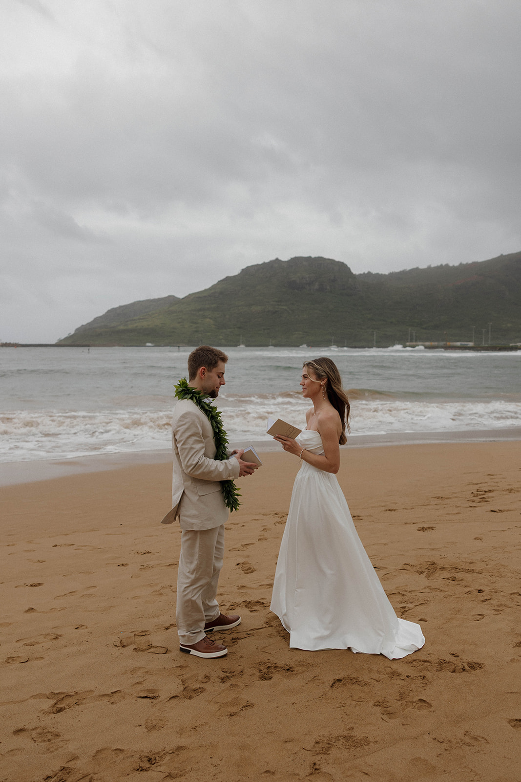 The bride reading her vows to her husband as they stand on the beach during their micro wedding in Kauai