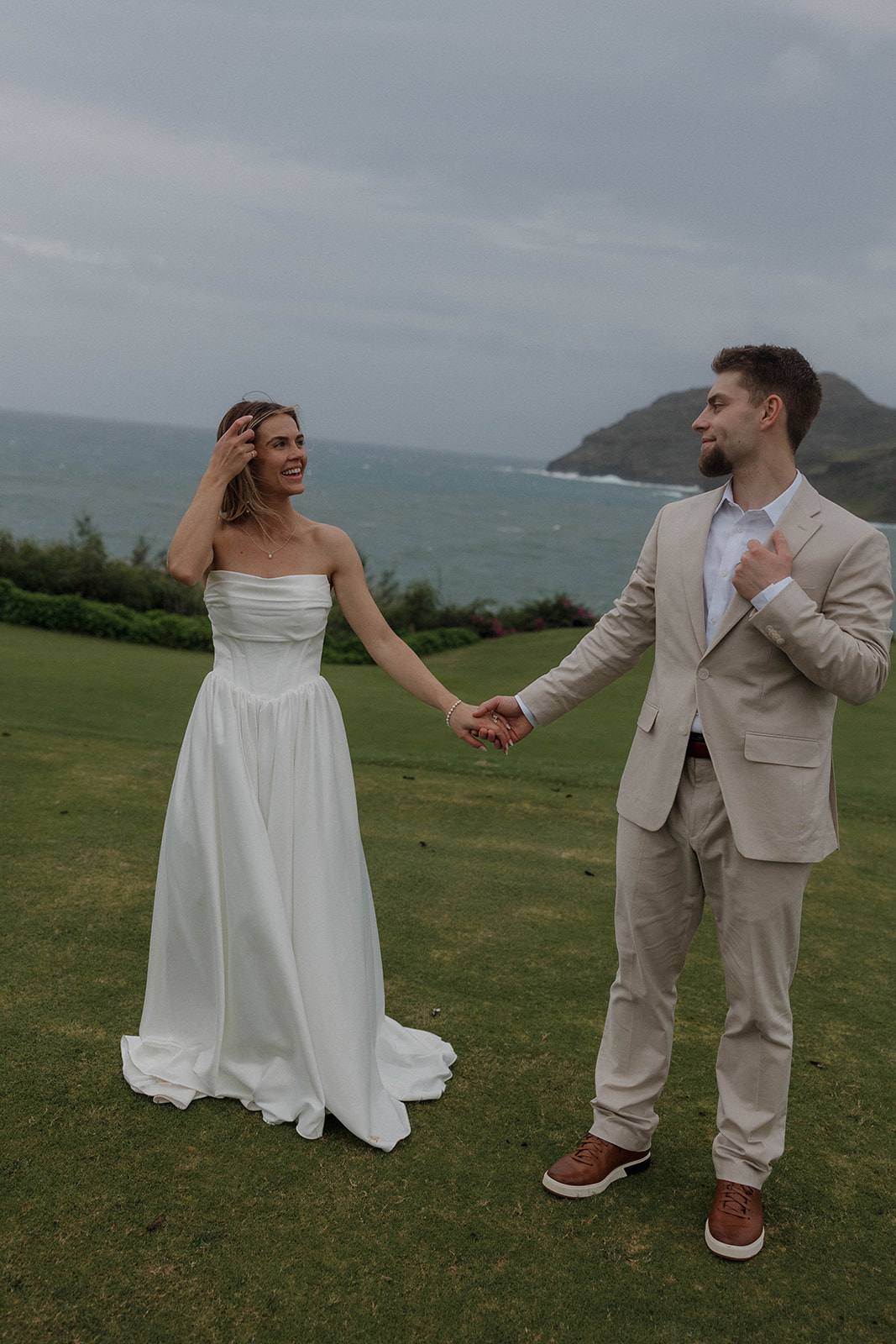 Newlywed couple holding hands on a coastal cliff overlooking the ocean at their micro wedding in Kauai
