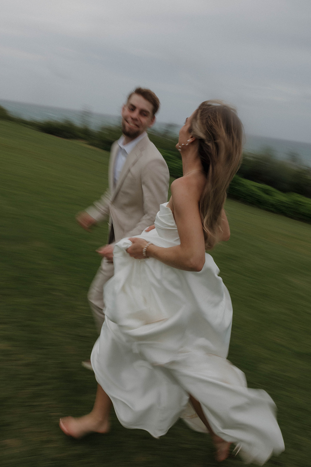 Coastal cliffside couples portraits of the couple candidly running around on the lawn, overlooking the ocean captured during a destination wedding in hawaii.