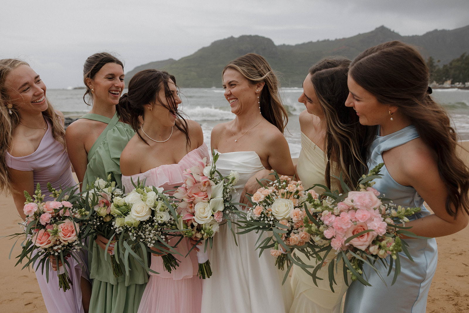 Bride standing an the beach with her bridesmaids in pastel dresses during her micro wedding in Kauai