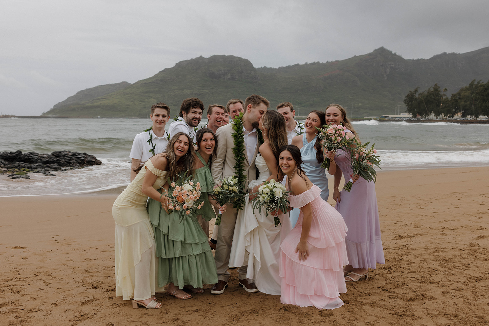 The bride and groom kissing on the beach with their wedding party surrounding them during their intimate micro wedding in Kauai