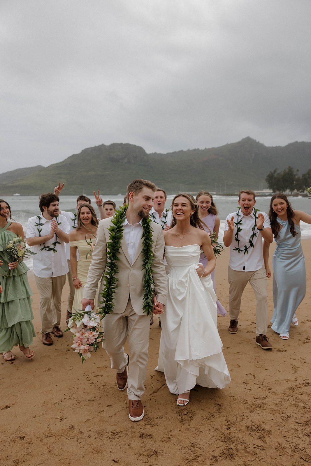 Joyful bridal party walking along the beach behind the bride and groom celebrating together by the water.